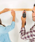 Two people using a drill to install a wooden beam on a wall.