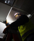 Electrician on ladder wearing Rechargeable Wide Beam Headlamp With Strap And 575 Lumens Five Lighting Modes All Day Runtime Direct Focus And Hard Hat Compatibility For Work And Outdoor Adventures, fixing ceiling panel.