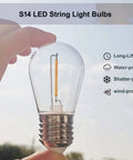 Hand holding S14 LED bulb outdoors showing shatterproof feature, part of 25 Pack Replacement LED Bulbs For S14 String Lights Shatterproof Waterproof