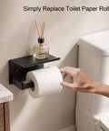 Rock Solid Matte Black Toilet Paper Holder With Storage Shelf Wall Mount For Bathrooms Fits Mega Rolls showing hand replacing toilet paper roll.