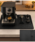 Straight Fire Premium Silicone Coffee Drip Mat With Built In Tamping Station, Non Slip Overflow Shield For Oster Perfect Brew, Heavy Duty Barista Counter Organizer And Quick Drainage Tray, Black placed under an espresso machine.