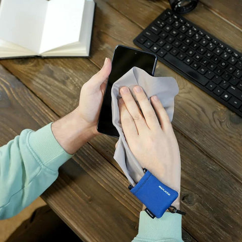 SPUDZ microfiber screen cleaner cloth in gray with blue pouch, front view of hands wiping a smartphone screen.