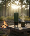 Ultra Portable Espresso Maker With Self Heating Tech On The Go next to a campfire, with a steaming mug, ideal for camping.