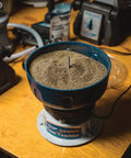 Quick N EZ Vibratory Case Tumbler with clear viewing lid on a wooden table, filled with dry media for brass cleaning.
