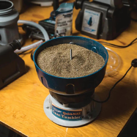 Quick N EZ Vibratory Case Tumbler with clear viewing lid on a wooden table, filled with dry media for brass cleaning.