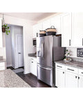 Modern kitchen with stainless steel fridge, white cabinets, black cabinet pulls, and granite countertops.