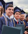 Group of graduates wearing royal blue and white graduation cords for 2026 with gowns and caps at commencement ceremony.