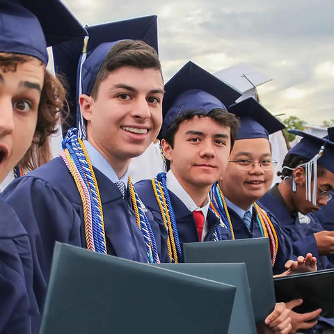 Group of graduates wearing royal blue and white graduation cords for 2026 with gowns and caps at commencement ceremony.