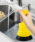 Hand holding a bright yellow Tiny 7 Inch Sink Plunger With Ergonomic Grip No Sweat Mini Clog Remover in kitchen sink