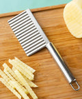 Front view of stainless steel vegetable and fruit wavy crinkle cutter on wooden cutting board.