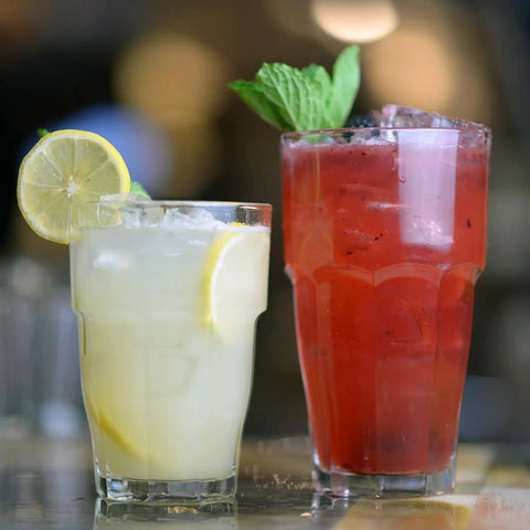 Two Rock Bar 16.25 Oz Cooler Glasses filled with colorful iced cocktails, garnished with lemon and mint, showcasing stackable design.