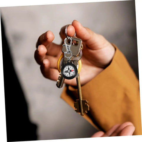 Hand holding keychain with Compact Hiking Compass Keychain With Snap Hook Lightweight Plastic Pocket Compass for navigation.