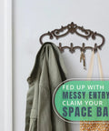 Knockout Five Hook Cast Iron Wall Hanger In Rustic Brown Fleur De Lis Farmhouse Entryway Coat Rack holding a green jacket and bag.