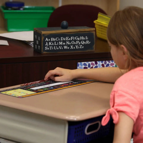 Student using Top Shelf Chalkboard Style K-2 Desk Reference Mats made of premium plastic on classroom desk.