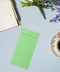 60 Pack Green Kraft Paper Coin Envelopes Self Seal With Double Adhesive Vintage Style Envelopes on a workspace with flowers and coffee.