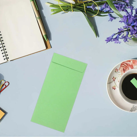 60 Pack Green Kraft Paper Coin Envelopes Self Seal With Double Adhesive Vintage Style Envelopes on a workspace with flowers and coffee.