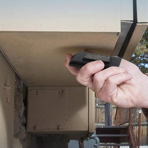 Hand placing a black 3-Pack Magnetic Key Lock Box Set With Strong Magnets For Car Home And Outdoor Use Hide A Spare Key under an outdoor surface.