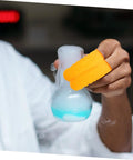 Person holding a lab beaker with smoke, wearing Top Shelf 100 Pack Yellow Latex Finger Sleeves Made To Straight Up Shield Blister Friction And Pain For Heavy Lifting Daily Tasks Smooth Moves And Maximum Grip Keep Digits Locked Safe With Zero Sweat.