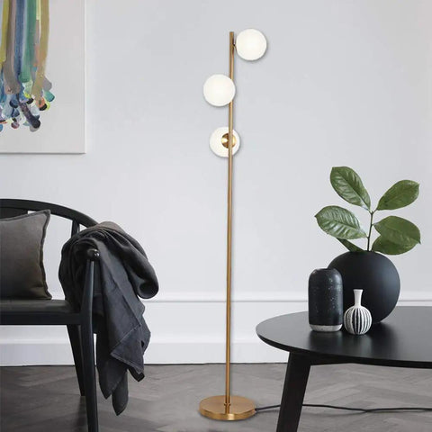 Three Globe Brushed Brass Floor Lamp, Modern LED Standing Light For Living Room, Bedroom, And Office in a cozy setting