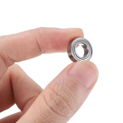 Close-up of Deep Groove Ball Bearings Set 5x8x2.5mm for Rollers and Skateboards held between fingers, double metal seals visible.