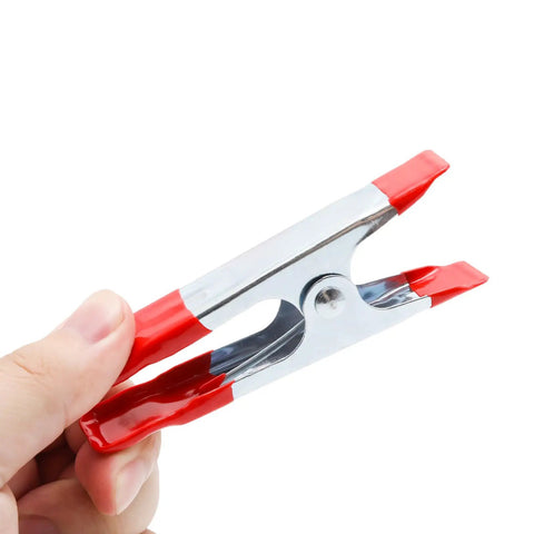 Rock Solid Four Inch Metal Spring Clamps With Grippy Rubber Tips held in hand, showcasing shiny metal and red rubber tips.