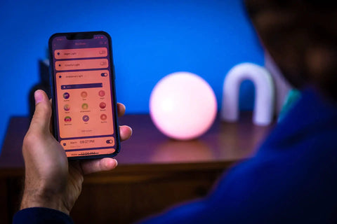 Person using smartphone app to control Smart Led Entertainment Lamp And Night Light With 16 Million Colors on nightstand.