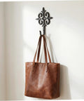Rock Solid Cast Iron Wall Hook Knockout Vintage Charm For Entryway And Master Bedroom Bullet Proof Heavy Duty Towel And Coat Rack Dead Simple No Sweat Installation In Matte Black Finish With Screws Included Now, holding a brown tote bag.