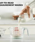 Pouring milk into Two Piece Glass Measuring Cups Set With 1 Cup And 2 Cup Sizes For Easy No Fuss Prep Baking And Cooking Oven Safe Microwave Safe Freezer Safe And Dishwasher Safe Clear Ounces And Milliliters Measurements For Fast Pouring.