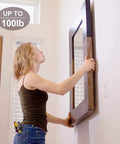 Person hanging a large mirror using heavy duty hanging screws for picture hangers, 100 lb capacity in wood studs.