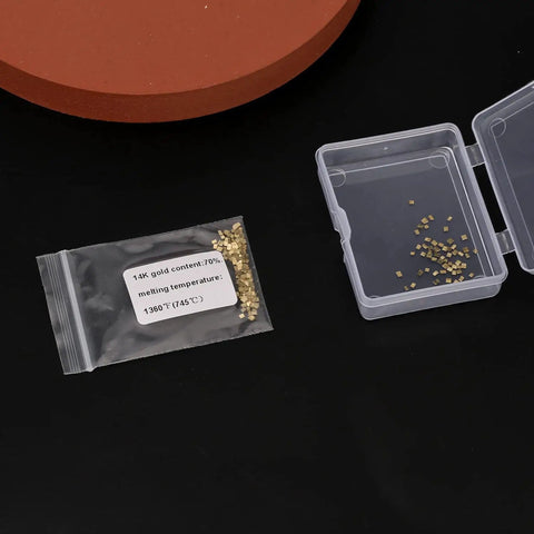 Gold-Plated Alloy Solder Chips 1x1mm, 0.5g Pack (About 200 Pieces) With 2% Gold in plastic and bag on dark surface