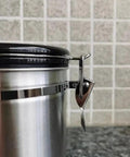 Close-up of Rock Solid 304 Stainless Steel Coffee Canister featuring snap tight closure and black lid on kitchen counter.