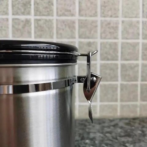 Close-up of Rock Solid 304 Stainless Steel Coffee Canister featuring snap tight closure and black lid on kitchen counter.