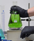 Person wearing Heavy Duty Black Nitrile Disposable Gloves 4 Mil Thick X Large 100 Count handling green liquid in laboratory flask.
