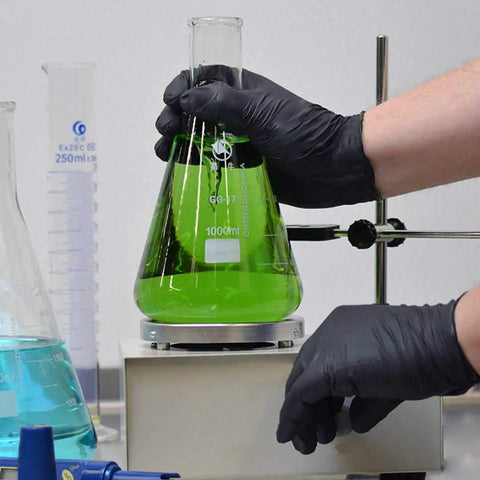 Person wearing Heavy Duty Black Nitrile Disposable Gloves 4 Mil Thick X Large 100 Count handling green liquid in laboratory flask.