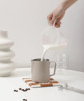 Stainless Steel Milk Frothing Pitcher With 14oz And 20oz Capacity For Latte Art on a table, milk being poured in, barista grade
