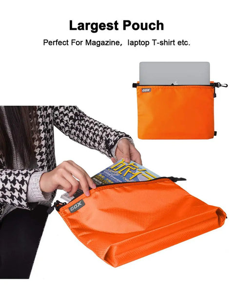 Large pouch from Three Pack Travel Toiletry Bags for Men Carry-On Organizer Pouch Set Zippered Cosmetic and Electronics Pouches Durable Nylon Ripstop Water-Repellent On-The-Go Portable Packing Cubes in Orange showing storage for magazines and laptop.