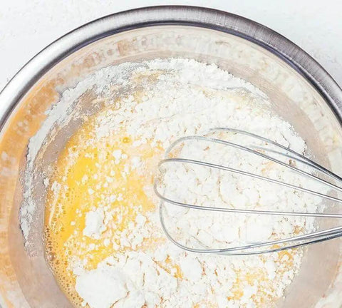 Killer Performance 400W Hand Blender With Versatile 3-In-1 Set Featuring Blending Shaft Whisk And Chopper Ergonomic Handle Adjustable Speed Control Effortless Mixing For Soups Smoothies And More Quick Rinse Design Black, mixing egg and flour in a stainless steel bowl.
