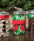 Glass jars filled with holiday candies, decorated with bows and festive designs, displayed under a Christmas tree.