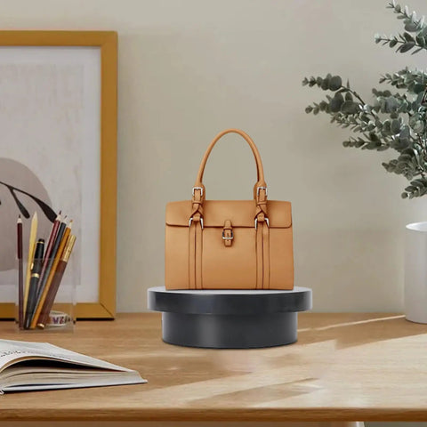 Cool Electric Turntable Display That Spins Your Goods 360 For Amazing Trade Fairs And Photo Shoots Plus It Runs On USB To Keep Things Easy And Green with tan handbag on a black base.