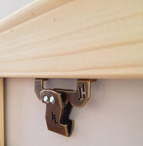 Close-up of 20 Lb Canvas Flat Mount Sawtooth Hangers 50 Pack Self Leveling Picture Hanging Hardware Antique Brass Finish on frame