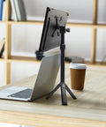 Metal Portable Monitor Stand Tripod With 360 Degree Ball Head Phone And Tablet Clamp on desk, next to laptop and coffee cup.