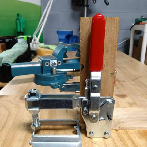 Badass Heavy Duty Vertical Toggle Clamps 10 Pack close-up on red lever clamp mounted on wood for industrial workholding and welding.
