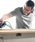 Heavy Duty 5 Inch Random Orbit Sander Featuring A Brushless Motor And Ergonomic Grip used on wooden surface by a person wearing safety glasses.