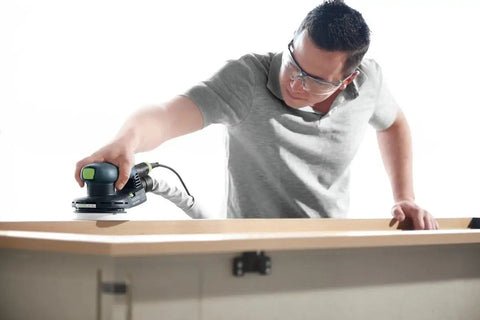 Heavy Duty 5 Inch Random Orbit Sander Featuring A Brushless Motor And Ergonomic Grip used on wooden surface by a person wearing safety glasses.