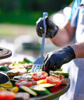 Person grilling vegetables wearing Heavy Duty Black Nitrile Disposable Gloves Tough As Nails For The Daily Grind And Auto Repair Seamless Grip Fit Powder Free Latex Free.