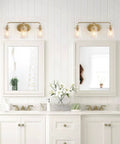 Bathroom with two white vanities and three light gold vanity light with seeded glass shades above mirrors.
