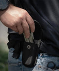 Person placing 13 In 1 Stainless Steel EDC Multitool with Nylon Sheath for Camping, Hiking, and Fishing into a belt pouch outdoors.