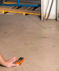 Green Laser Distance Measure Tool With 200 Foot Range For DIY And Pros in use on a concrete floor, showing green laser line.
