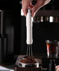 Dope Pink Magnetic Telescopic Coffee Distribution Needle And Rock Solid Stainless Steel Espresso Grounds Leveler for zero clumping, in hand over coffee grounds.