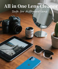 Camera with lens on a wooden desk, beside sunglasses, tablet, blue smartphone, mirror, and a cactus